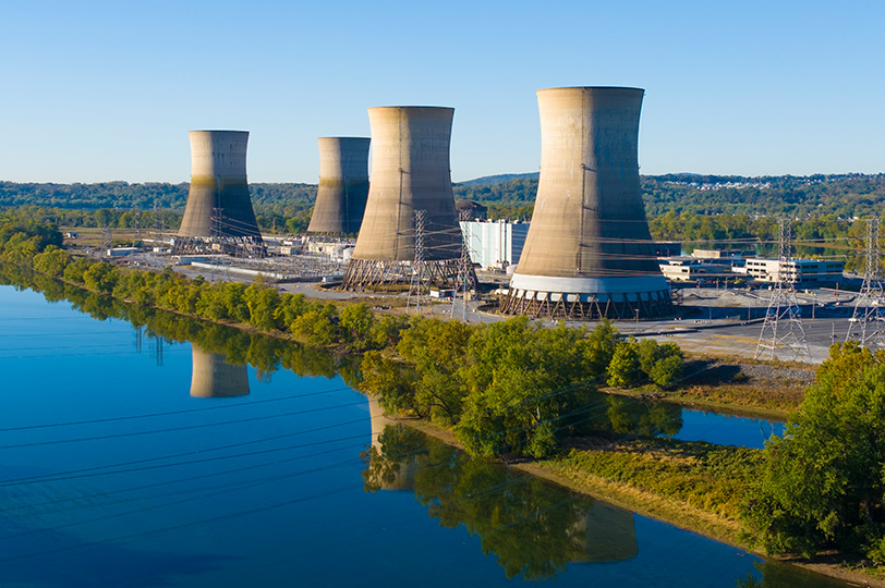 wide shot of 4 cooling towers along river during the day